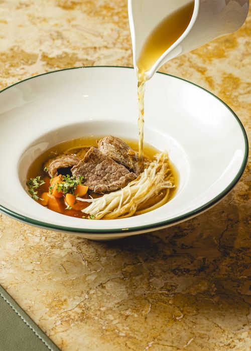 Beef consommé with vegetables, enoki mushrooms and rice noodles